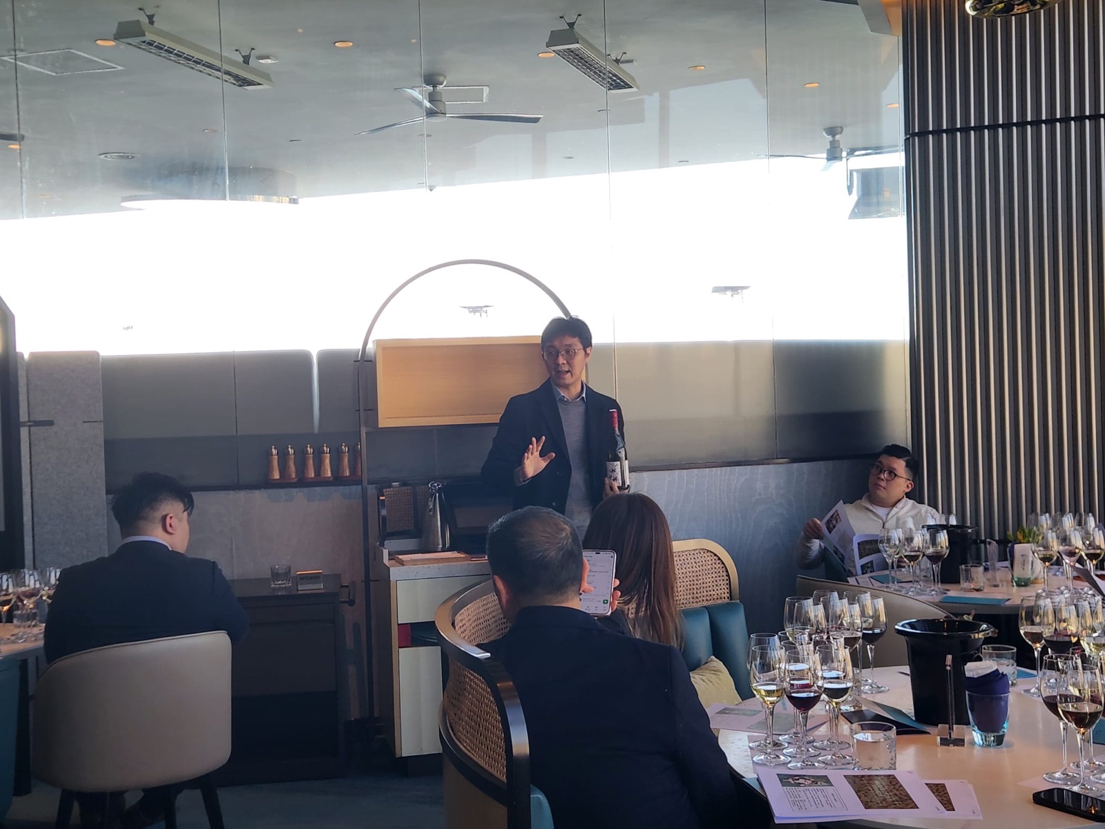 A speaker presenting a bottle of wine to guests at a tasting